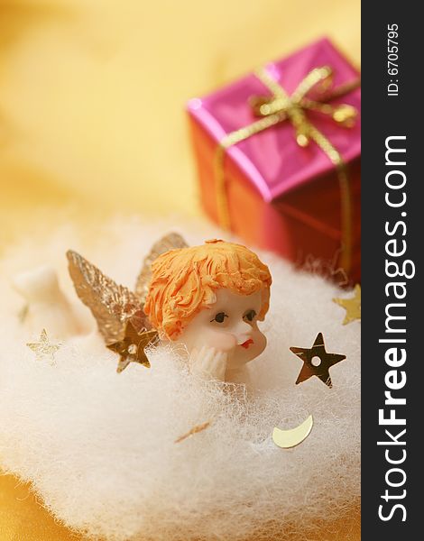 Angel on white cloud with golden stars and christmas gift with golden ribbon on golden background.