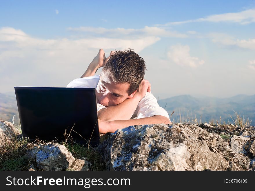Young man using his laptop, lying on the rock. Young man using his laptop, lying on the rock