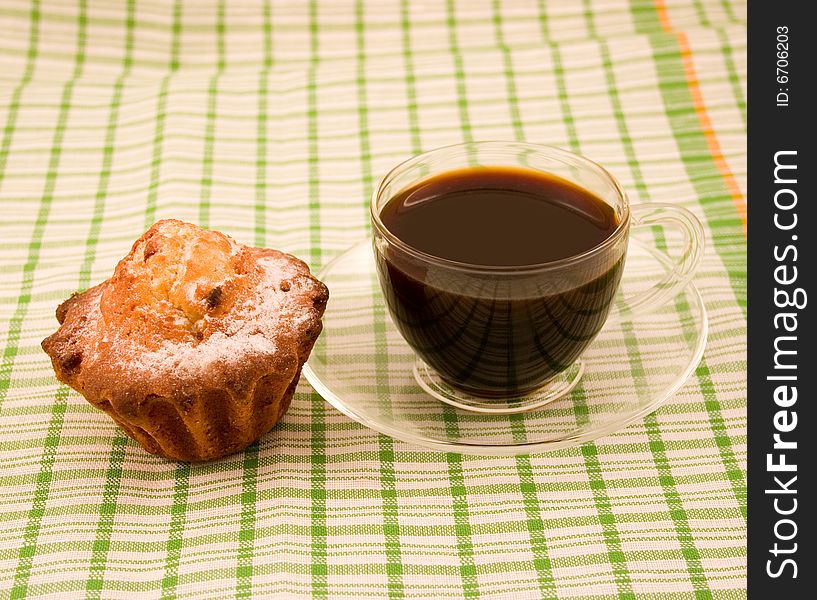 Biscuit fruitcake with powdered sugar and black coffee in transparent cup in green napkin strip