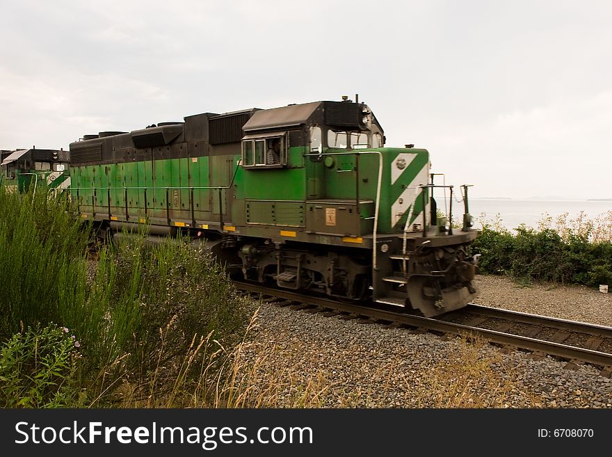 A speeding green locomotive along the edge of the sea. A speeding green locomotive along the edge of the sea