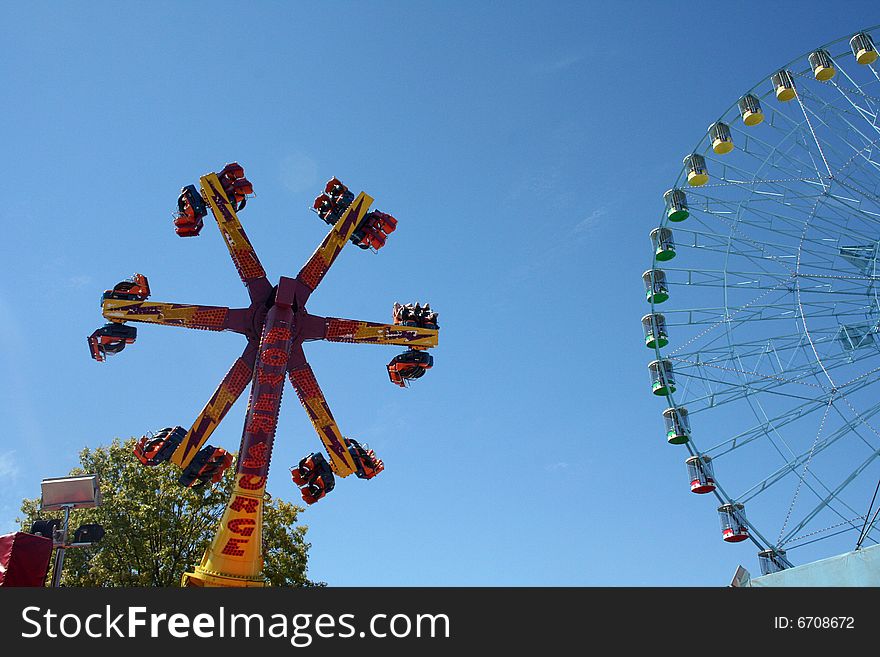 A carnival ride turns in circles against the blue sky.