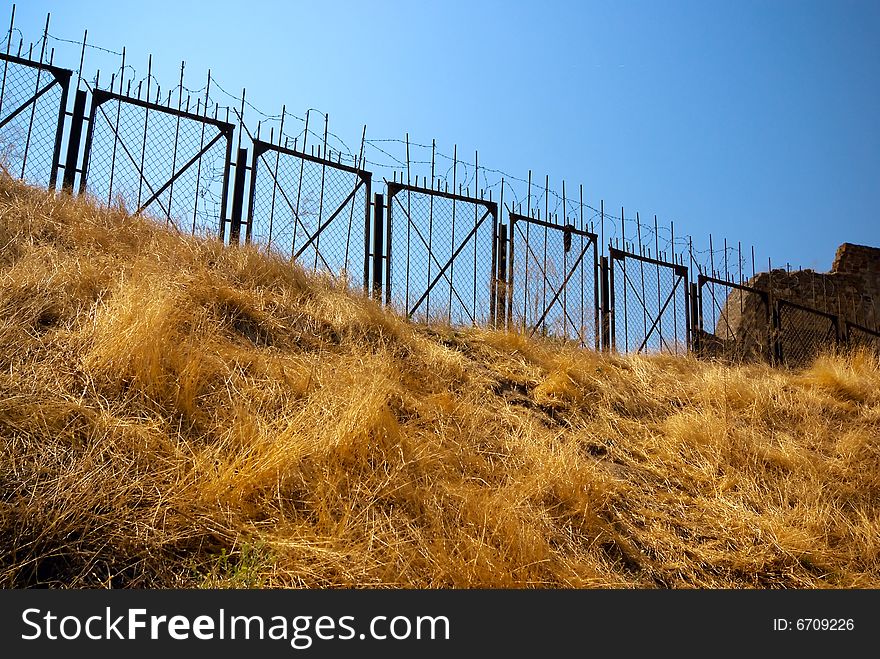 Barbed wire protects restricted area on the hill with yellow grass