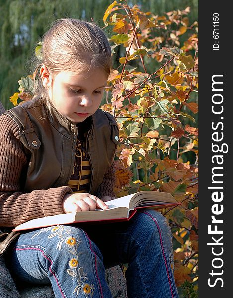 Little girl sitting on the stone and reading a book in the park. Little girl sitting on the stone and reading a book in the park