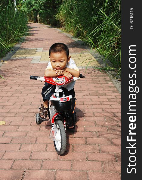 A naughty Chinese boy riding a bicycle on the footpath way in a park. A naughty Chinese boy riding a bicycle on the footpath way in a park.