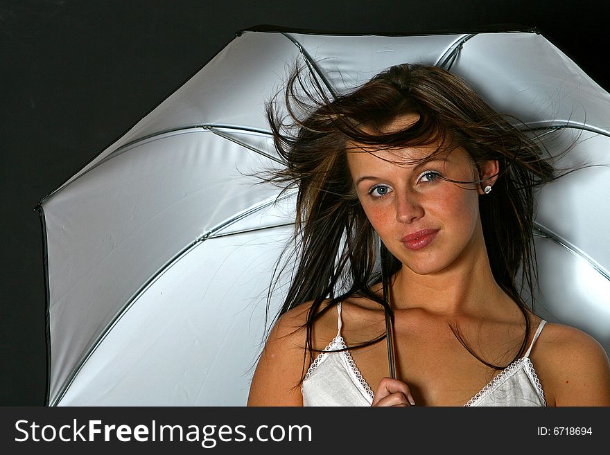 Beautiful gorges girl/young woman with long dark hair blown with wind holds white umbrella against black back-ground. Beautiful gorges girl/young woman with long dark hair blown with wind holds white umbrella against black back-ground