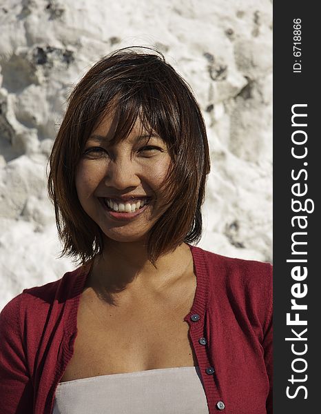 Happy smiling Asian woman at seaside. Shot at against White chalk cliffs.