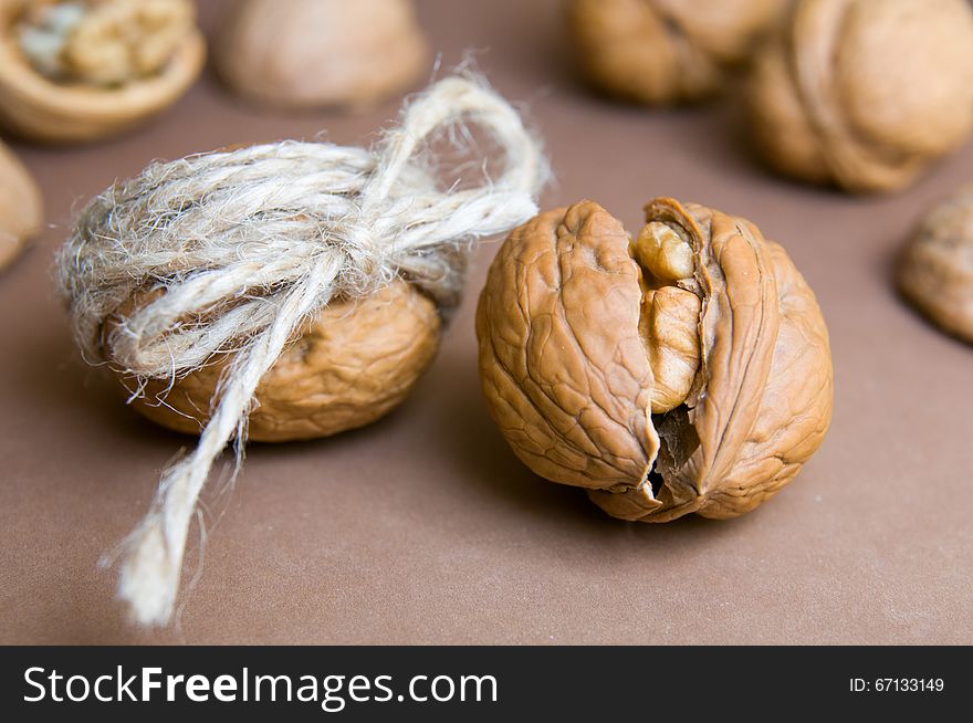 Walnut tied with twine and cracked walnut on the background of other blurry walnuts on a brown background. Brown, Beige colors