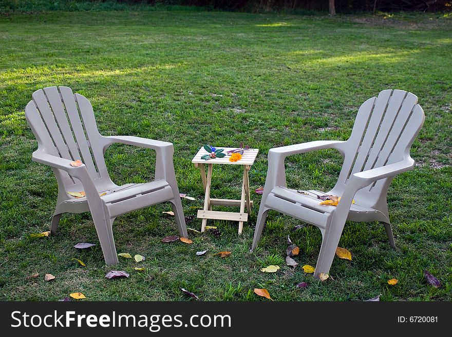 Two lounge chairs and a wooden table. Fall foliage, flowers, and berries scattered around. Two lounge chairs and a wooden table. Fall foliage, flowers, and berries scattered around.