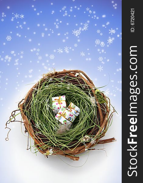 Conceptual image showing three presents in a bird's nest against a snowy background. Space for copy. Conceptual image showing three presents in a bird's nest against a snowy background. Space for copy.