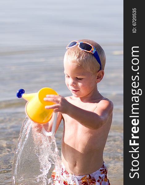 Boy pouring water from  his bucket at the beach