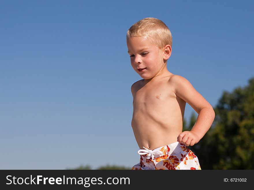 Boy walking at the beach with a clear blue sky above him