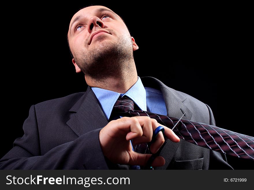 Man in a business suit scissors the tie, on a black background. Man in a business suit scissors the tie, on a black background