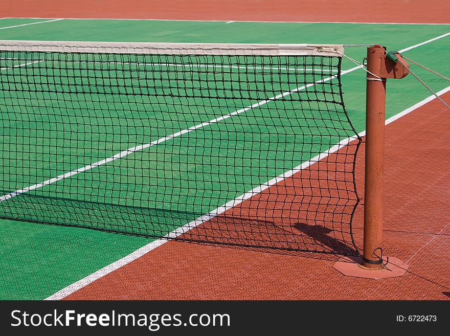 Green and brown tennis court with a post and a net. Green and brown tennis court with a post and a net