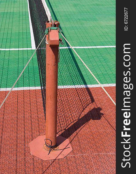 Green and brown tennis court with a post and a net. Green and brown tennis court with a post and a net