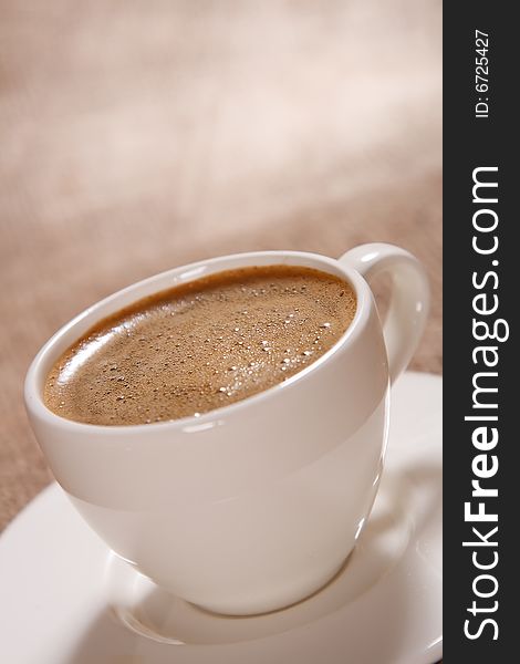 Cup of black coffee with froth on brown background, shallow DOF