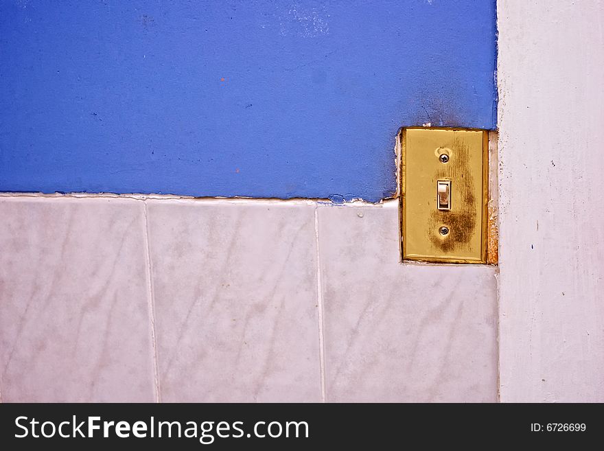 Old worn light switch with scratched brass cover on half tiled wall in need of repair