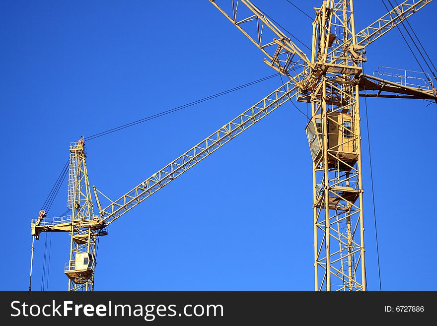 Two yellow cranes crossing on background with blue sky. Two yellow cranes crossing on background with blue sky