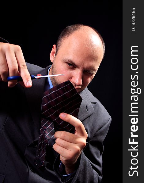 Man in a business suit scissors the tie, on a black background. Man in a business suit scissors the tie, on a black background