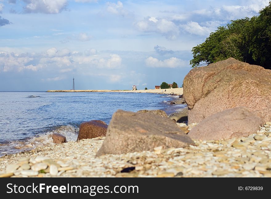 Pebbly sea coast, blue sky with clouds and water