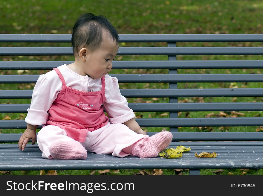 Chinese baby girl sitting on a park bench. Chinese baby girl sitting on a park bench