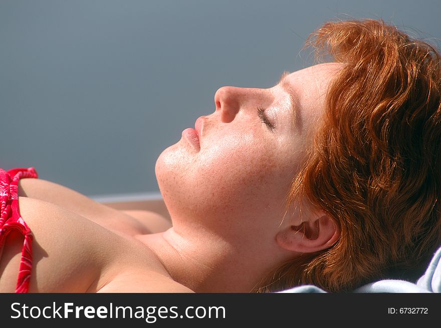 A young woman enjoys a quiet, peaceful afternoon and tans while laying on a boat out on a lake. A young woman enjoys a quiet, peaceful afternoon and tans while laying on a boat out on a lake.