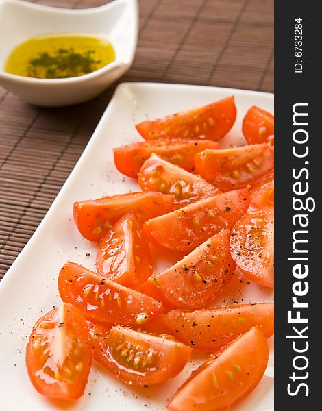 Sliced tomato on a plate with a bowl of fresh olive oil