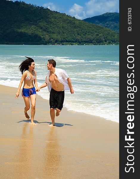 Couple running on beach holding hands smiling. Couple running on beach holding hands smiling