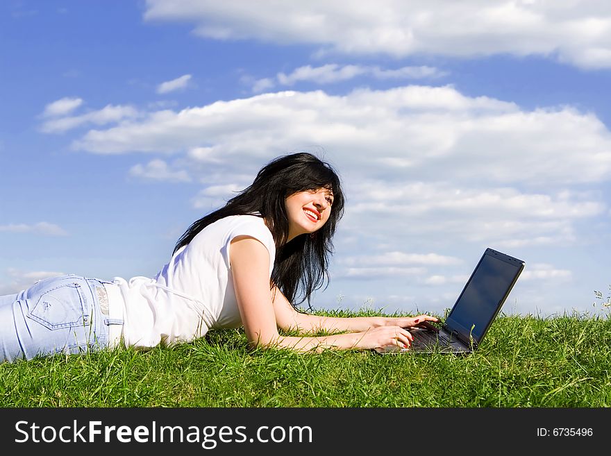 Pretty woman with laptop on the green grass