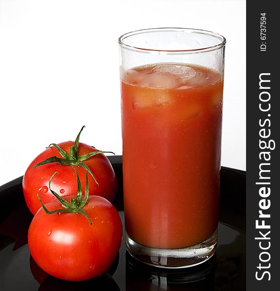 A glass of tomato juice and a fresh tomato on black background