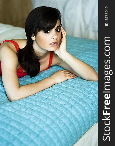 Beautiful woman relaxing on a bed. She is wearing a red top.