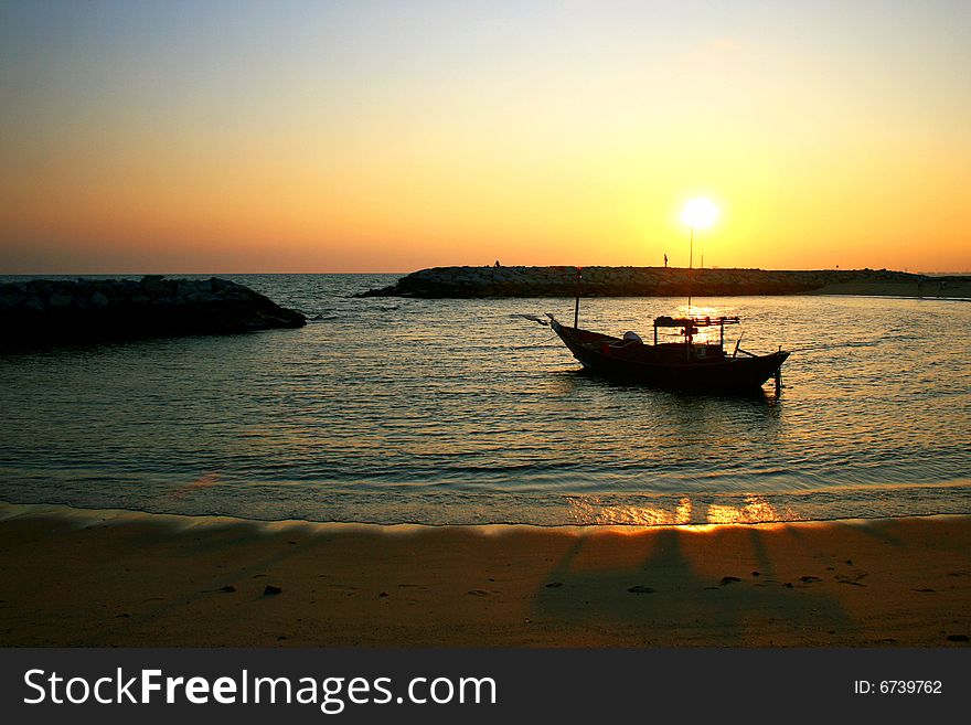 This small fisher boat floating on the sea near a beautiful beach in Rayong, Thailand with the sunset behind. This small fisher boat floating on the sea near a beautiful beach in Rayong, Thailand with the sunset behind