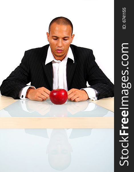 Young businessman sitting in front of a red apple thinking. Isolate over white. The table mirrors the image creating a nice effect!. Young businessman sitting in front of a red apple thinking. Isolate over white. The table mirrors the image creating a nice effect!