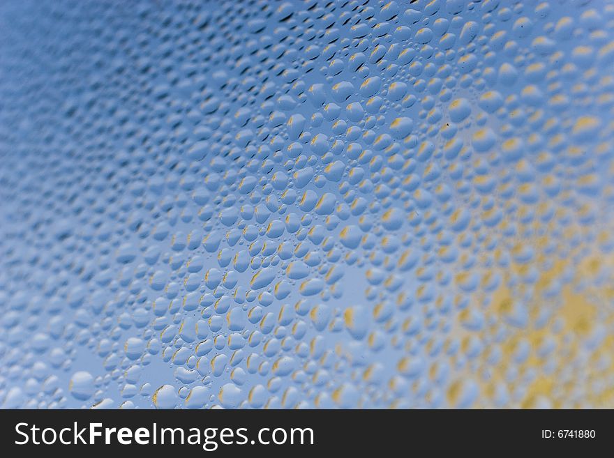 Slightly blurred abstract background (raindrops on blue glass with reflections of flying yellow autumn leaves)