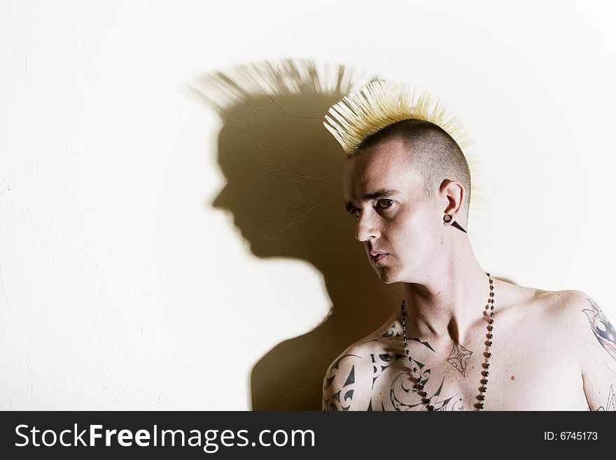 Punk with tattoos leaning against a white wall