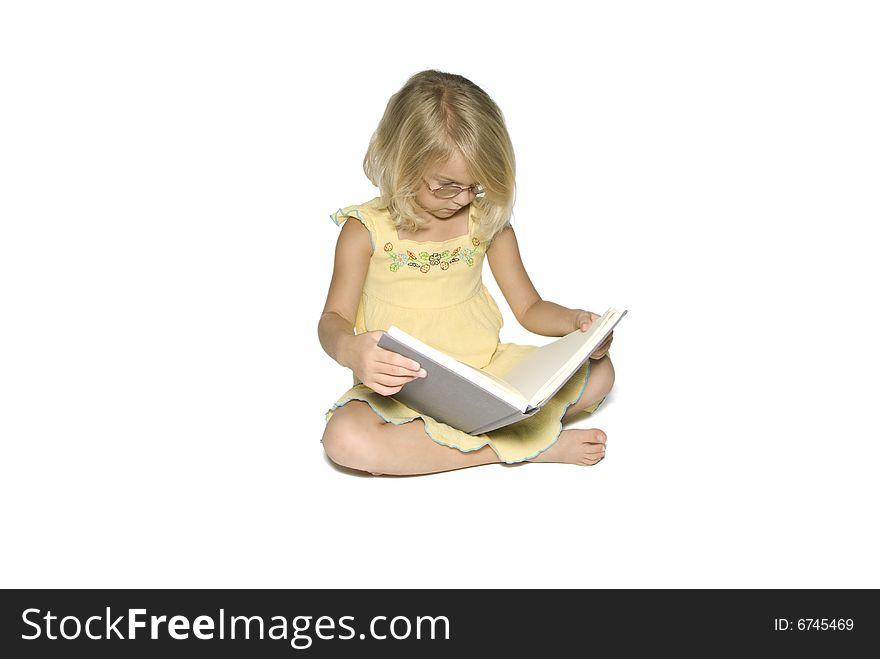 A young blonde girl sitting crosslegged while reading a textbook. Isolated on a white background. A young blonde girl sitting crosslegged while reading a textbook. Isolated on a white background