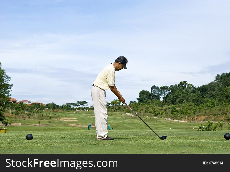 A Chinese pensioner driving off the blue tee box. A Chinese pensioner driving off the blue tee box