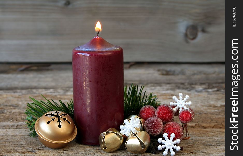 A lit candle with bells, snowflakes, evergreen and a wood textured background for a rustic look. A lit candle with bells, snowflakes, evergreen and a wood textured background for a rustic look.