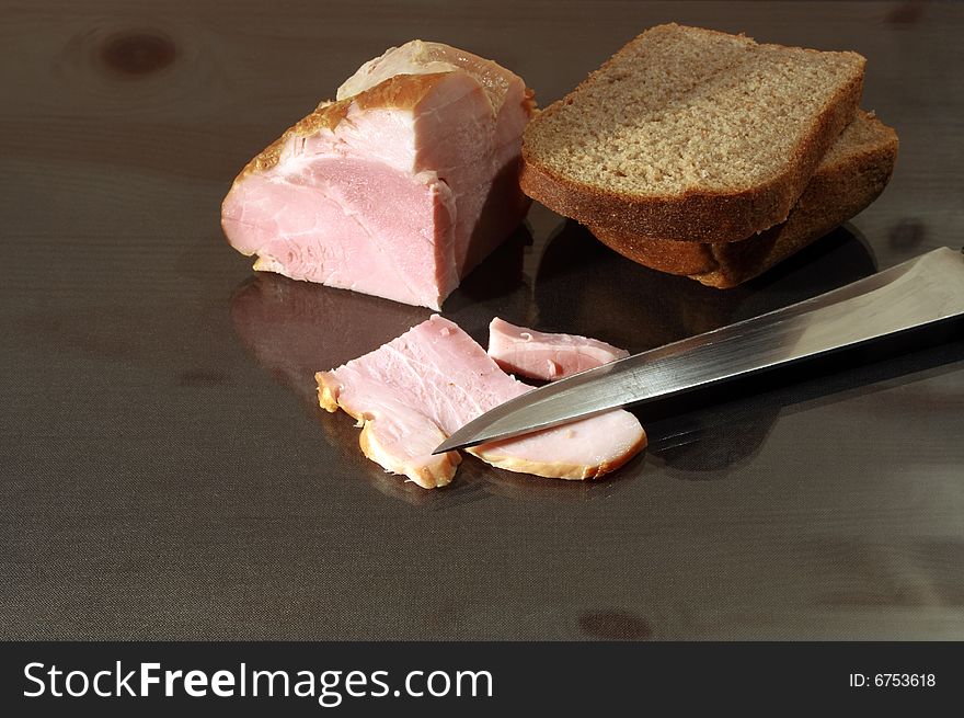 Slit ham and rye bread with kitchen knife on glassy table. Slit ham and rye bread with kitchen knife on glassy table