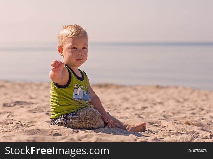 Young boy sitting in the sand and waving at the beach. Young boy sitting in the sand and waving at the beach