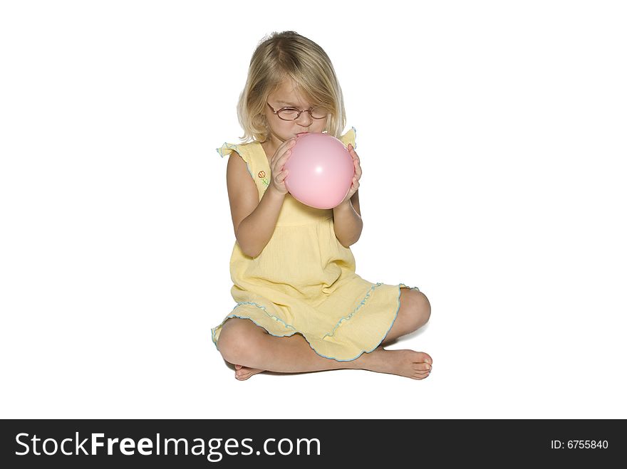 A young girl in a yellow dress sitting down and blowing up a pink balloon.  Isolated on a white background. A young girl in a yellow dress sitting down and blowing up a pink balloon.  Isolated on a white background