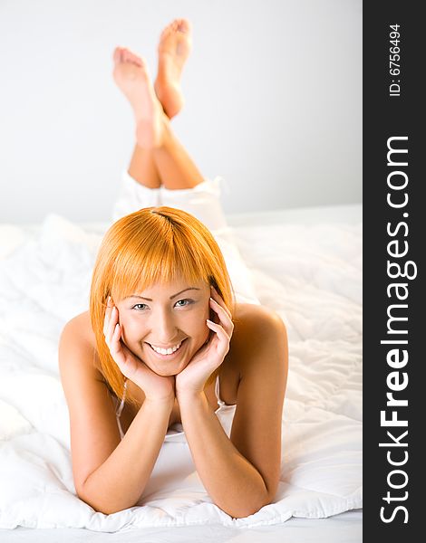 Young red-haired woman lying in bed. She's smiling and looking at camera. High angle view. Young red-haired woman lying in bed. She's smiling and looking at camera. High angle view.