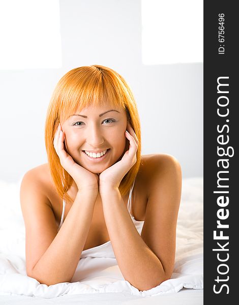 Young red-haired woman lying in bed. She's smiling and looking at camera. Front view. Closeup on face. Young red-haired woman lying in bed. She's smiling and looking at camera. Front view. Closeup on face.