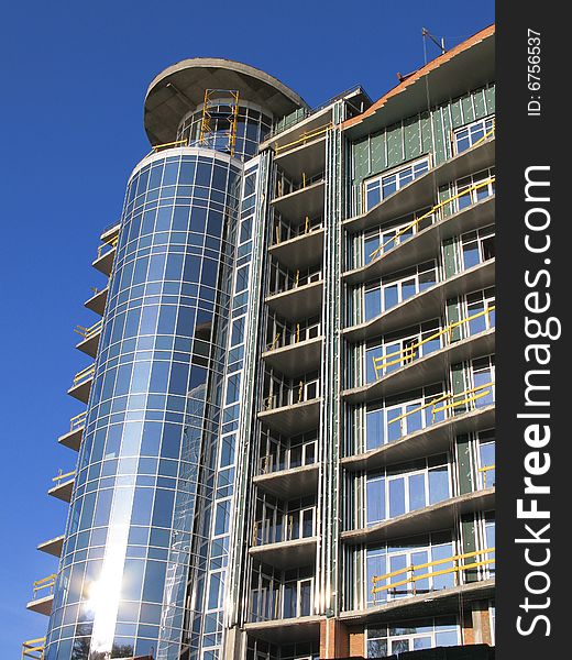 The Construction of the building. The Sun sparkles in new glass, on background blue sky.