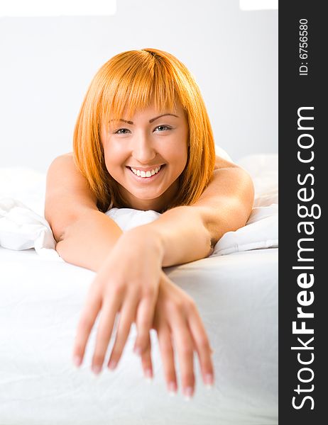 Young red-haired woman lying in bed. She's smiling and looking at camera. Front view. Young red-haired woman lying in bed. She's smiling and looking at camera. Front view.