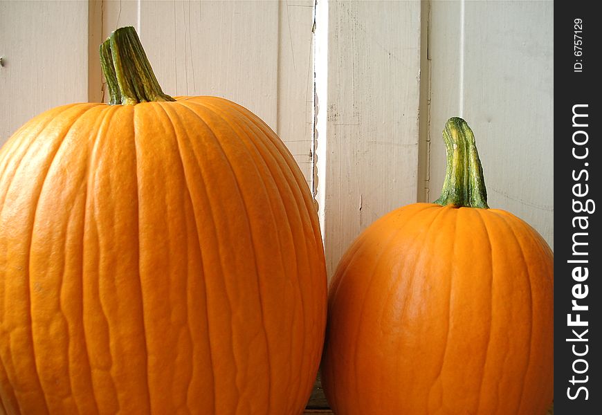 Two pumpkins sitting next to an old, white door.