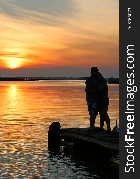 Bride and groom standing on their dock gazing at the sunset hours away from the wedding day. Bride and groom standing on their dock gazing at the sunset hours away from the wedding day