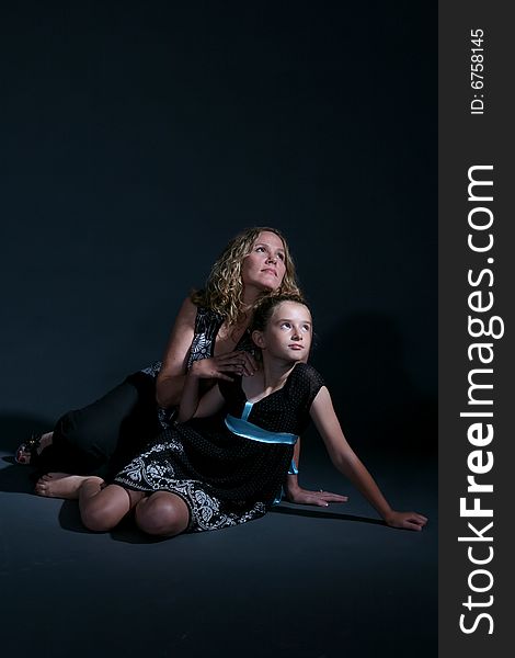 Mother and daughter on the floor together on a dark background. Mother and daughter on the floor together on a dark background