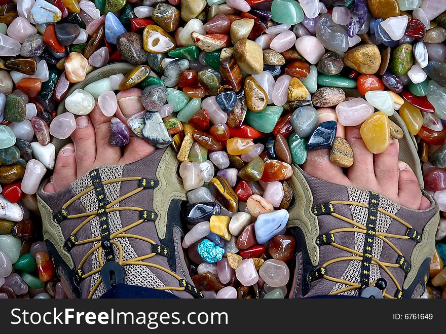 Feet at sandal footwear standing on coloured grinded semiprecious background. Feet at sandal footwear standing on coloured grinded semiprecious background