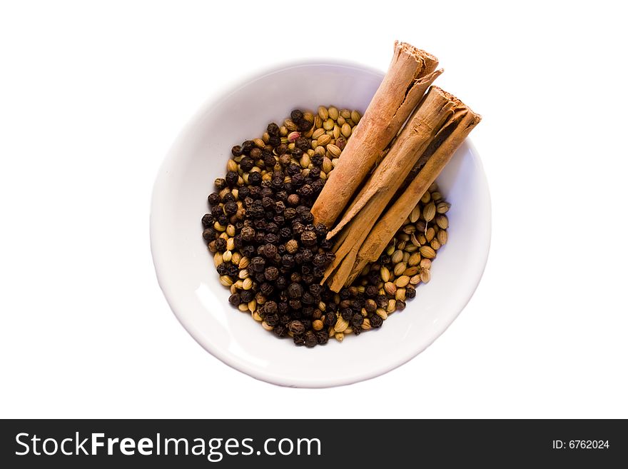 Coriander seeds, black peppercorns and two cinnamon sticks in white porcelain bowl on white background. Coriander seeds, black peppercorns and two cinnamon sticks in white porcelain bowl on white background