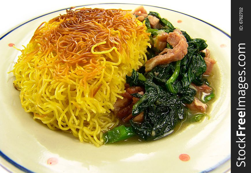 Closeup of a dish of Chinese fried noodles with green vegetable and ham on a ceramic plate. Closeup of a dish of Chinese fried noodles with green vegetable and ham on a ceramic plate